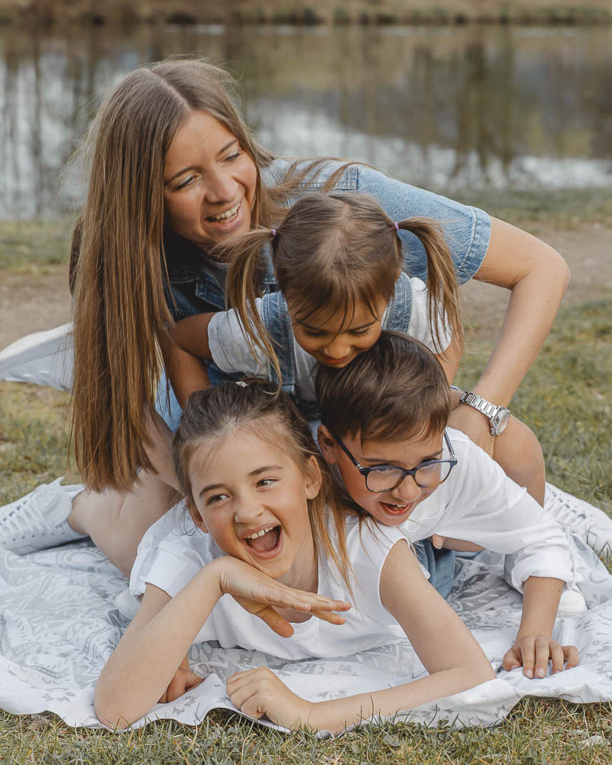 Familienfotografie Regensburg - eine Mama mit ihren drei Kindern - alle purzeln fröhlich übereinander.