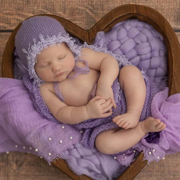 Schlafendes Baby in lila Stoffen im Holzkörbchen